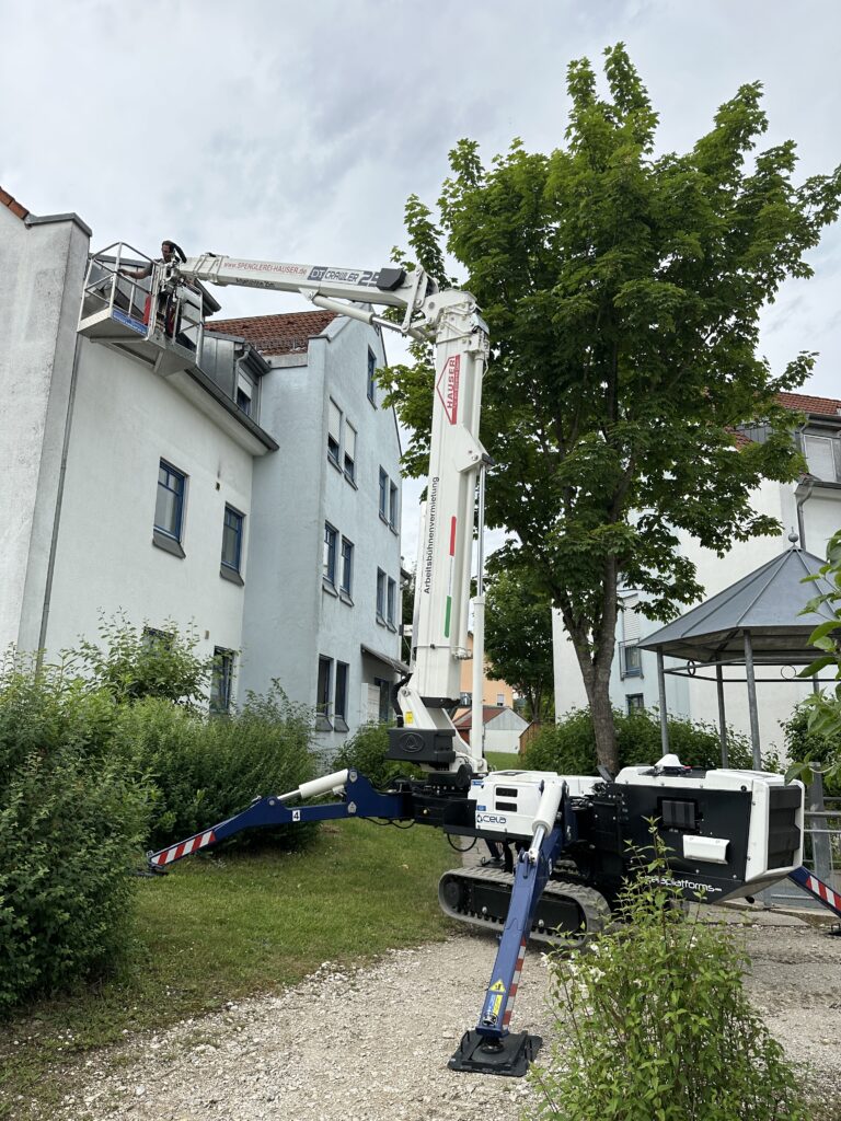 Teleskop-Raupenbühne mit ausgefahrenem Arm vor einem Gebäude zur Dachwartung